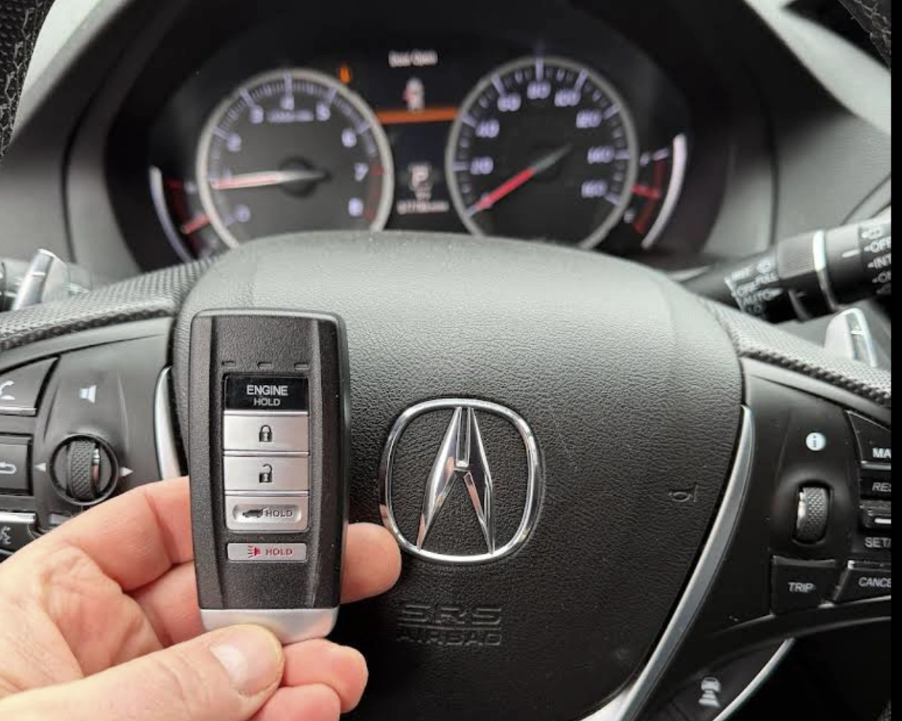 Freshly programmed Acura smart key held in front of the Acura steering wheel airbag with the Acura emblem visible