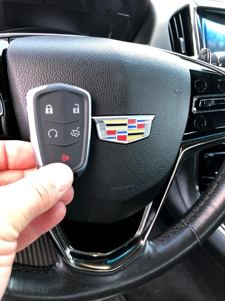 Freshly programmed Cadillac smart key held in front of the Cadillac shield emblem on the steering wheel airbag with the brand's signature multi-color crest visible