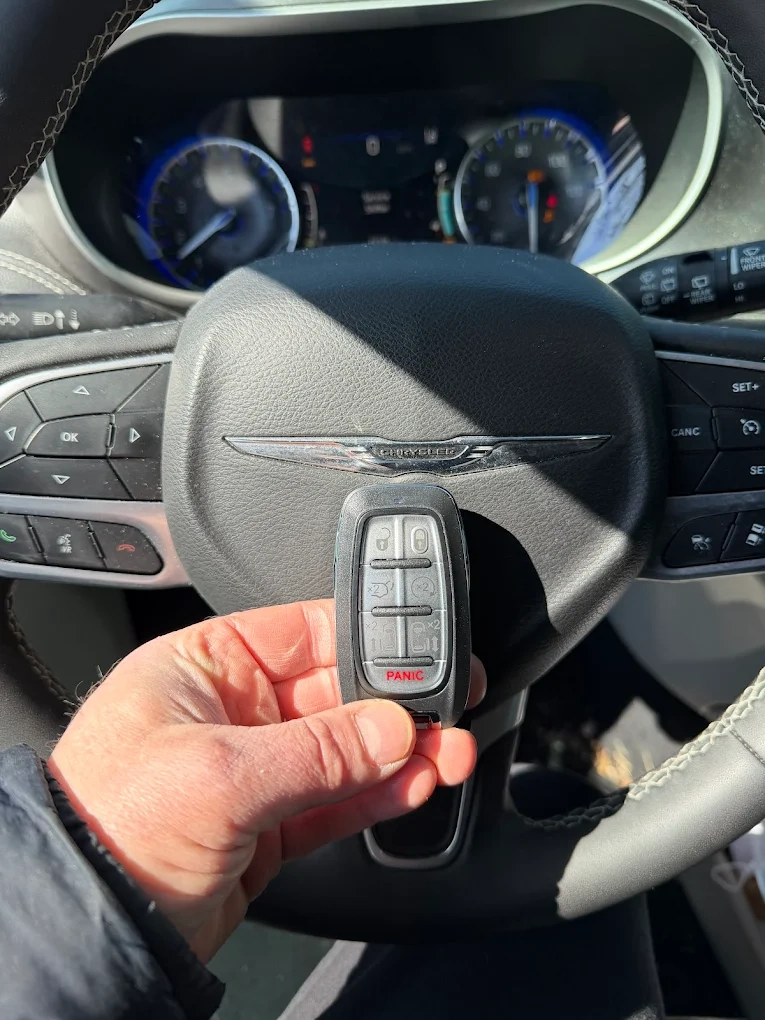 Freshly programmed Chrysler Pacifica 7-button minivan smart key (with sliding-door and liftgate controls) held in front of the chrome Chrysler wings emblem on the steering wheel airbag