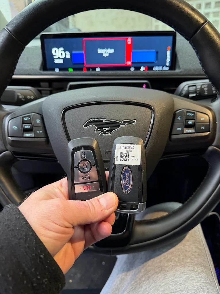 Pair of Ford Mustang smart keys held in front of the Mustang steering wheel airbag with the iconic running pony emblem and a digital instrument cluster visible