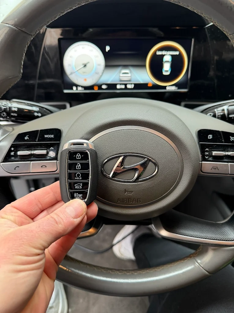 Freshly programmed Hyundai smart key held in front of the Hyundai steering wheel emblem with the digital instrument cluster visible behind