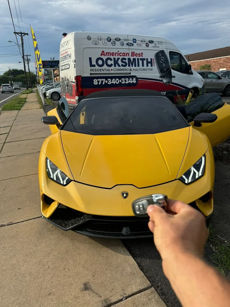 Freshly programmed Lamborghini Huracán smart key held in front of a yellow Lamborghini Huracán with the American Best Locksmith service van behind showing the brand emblems we service and the 877-340-3344 phone number