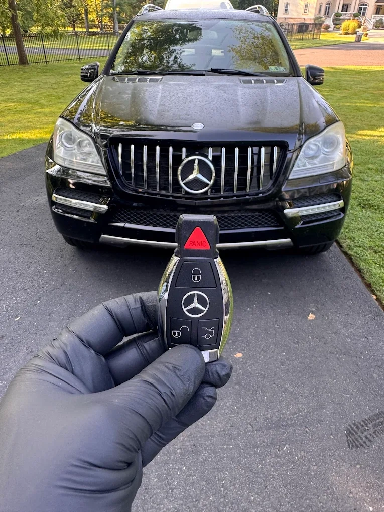 Freshly programmed Mercedes-Benz fish-style smart key held in gloved hand in front of a black Mercedes-Benz ML350 SUV at a customer's driveway