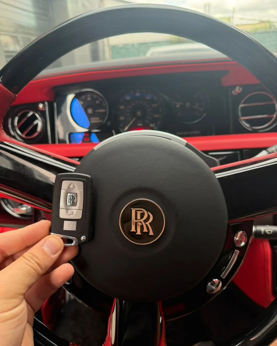 Rolls-Royce smart key held against the steering wheel of a 2009 Rolls-Royce Phantom with red leather interior and the RR emblem on the wheel